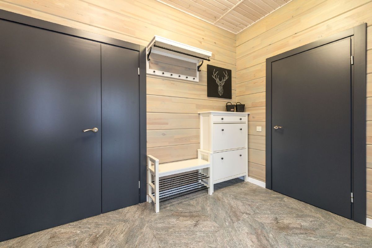 White shoe storage cabinet with a slatted bench and open shoe rack beneath it, set against a pale wood-panelled entryway wall
