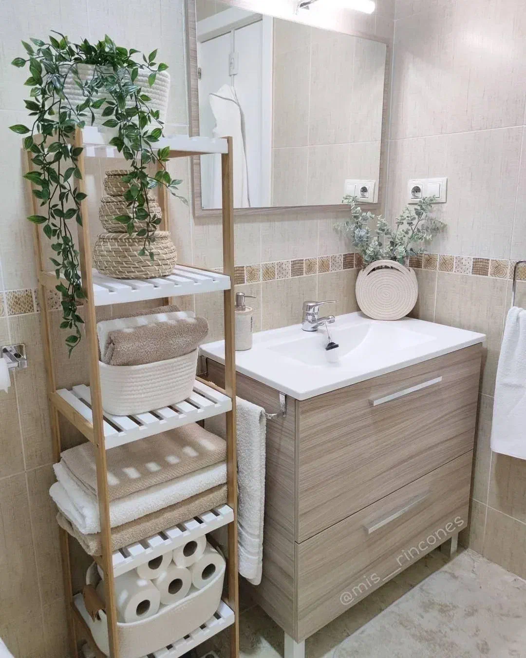 Small bathroom with a light wood vanity, simple mirror, and a vertical wooden shelving unit for optimized storage.