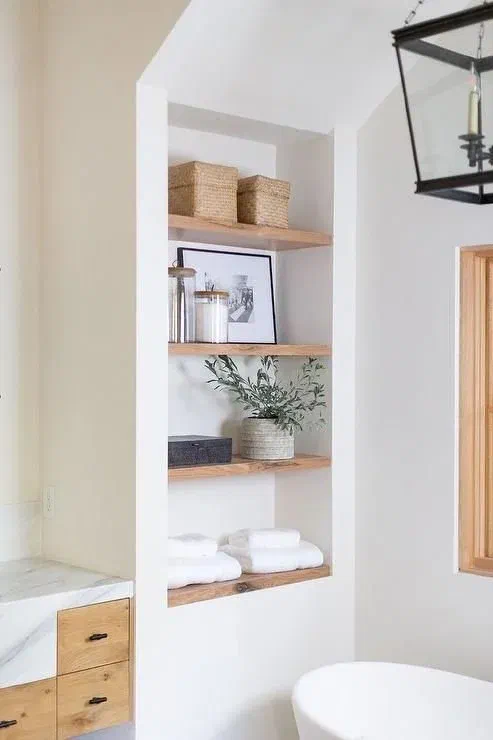 Recessed nook shelving with natural wood shelves in a bathroom, displaying baskets and neatly folded towels.