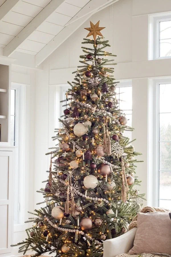 Christmas tree trimmed in mauve, bronze, and gold ornaments with tasseled garland and a gold star topper