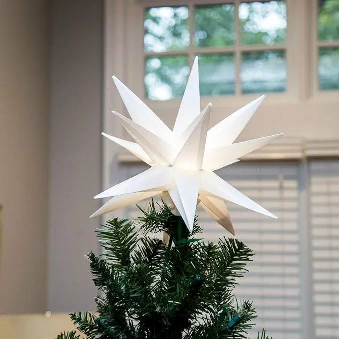 Warm white LED Moravian star tree topper glowing atop a Christmas tree in front of a window