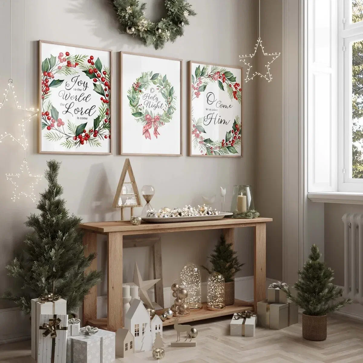 Three framed Christmas carol wreath prints hung above a console table styled with mini trees and gifts