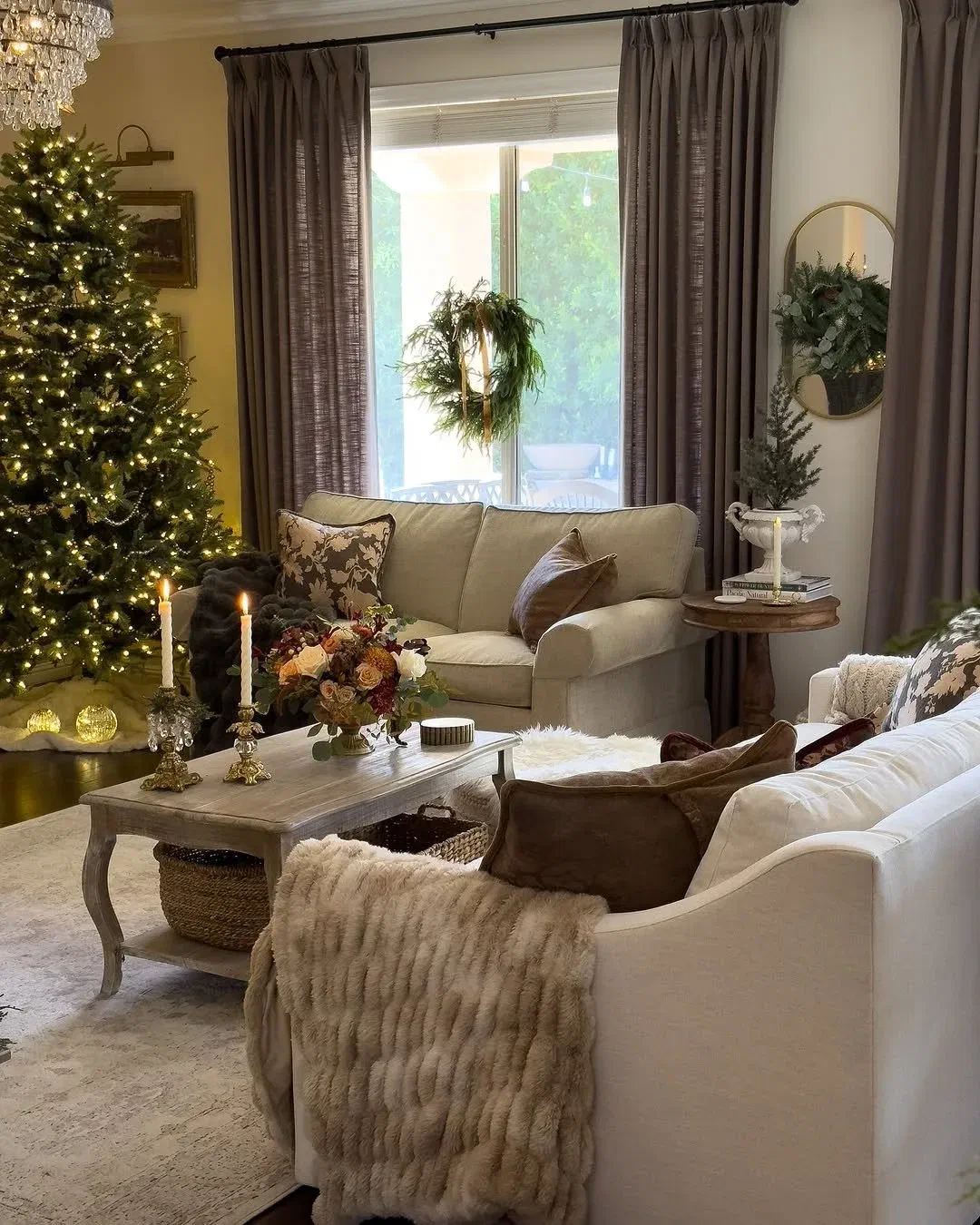 Simple greenery wreath hung in a window above a cozy living room with a lit Christmas tree and candlelit coffee table