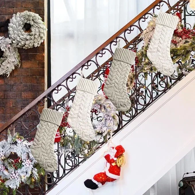 Cream cable-knit Christmas stockings hanging from a staircase railing decorated with flocked garland