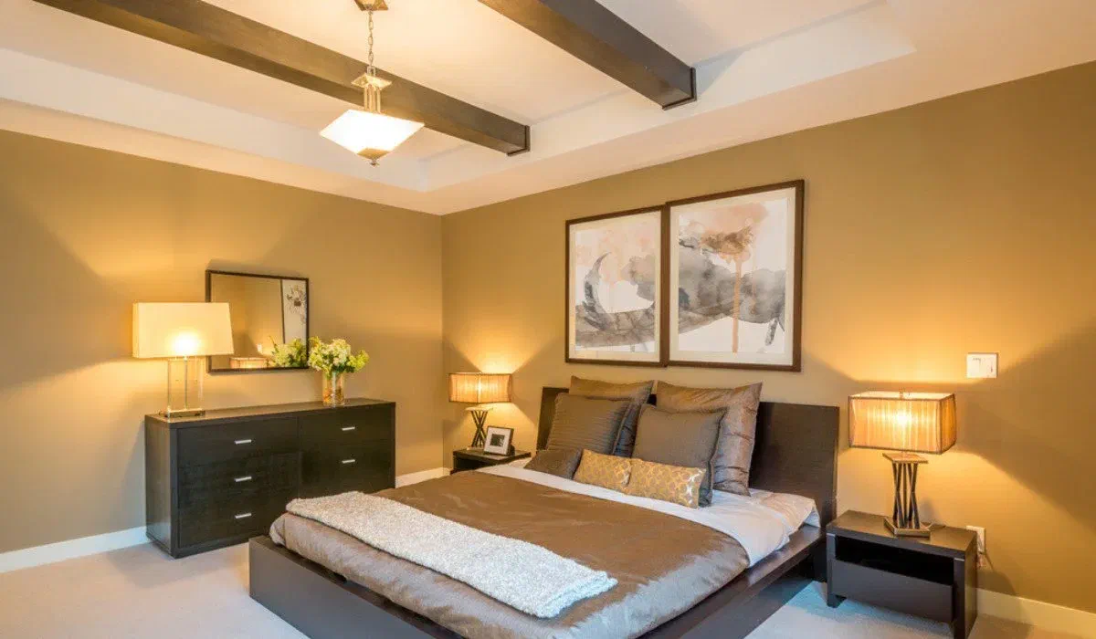 A bedroom with layered lighting: ambient ceiling fixture, task lamps on nightstands, and accent light highlighting artwork, showcasing different bedroom lighting ideas.