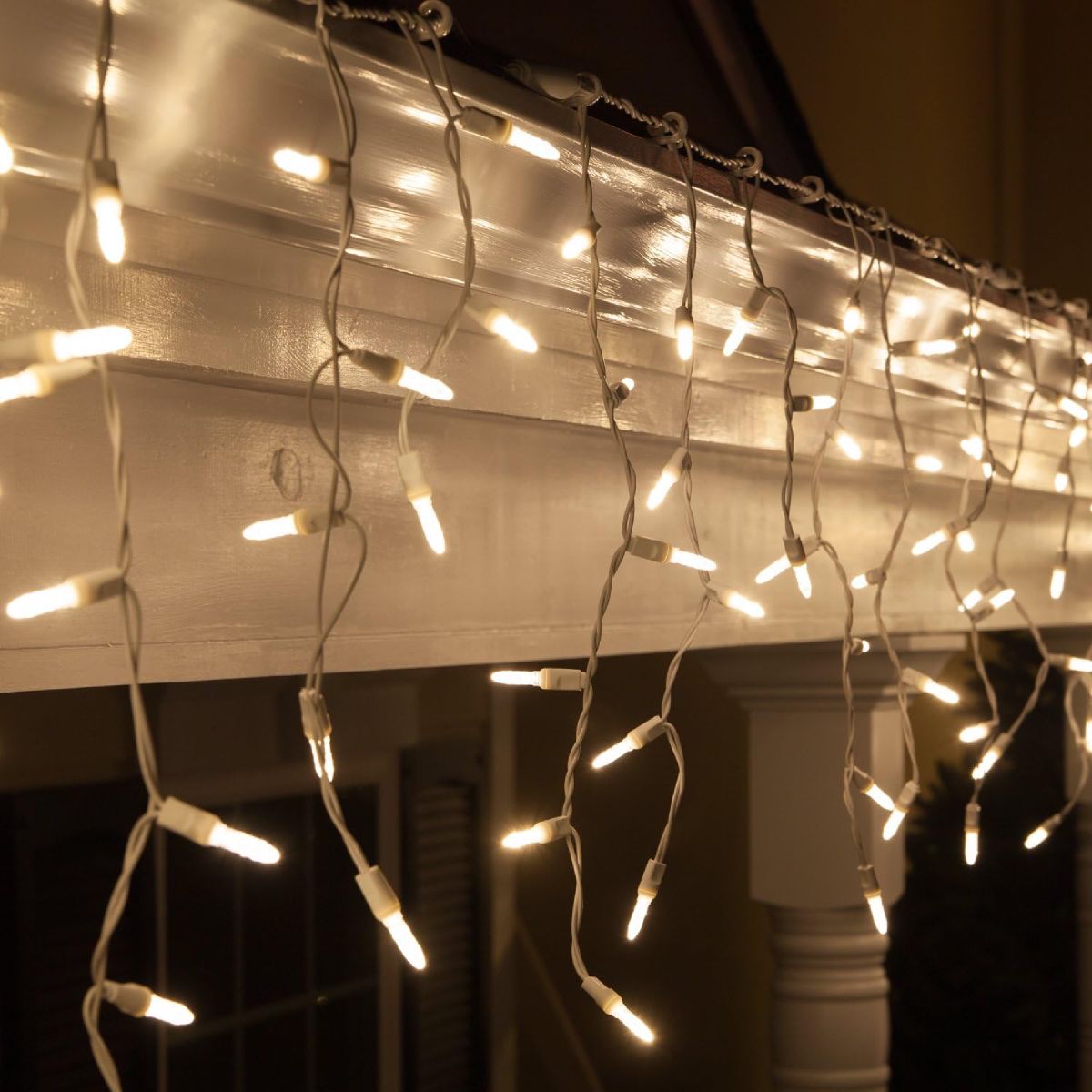Warm white icicle lights hanging in uneven cascading drops along a roofline at night