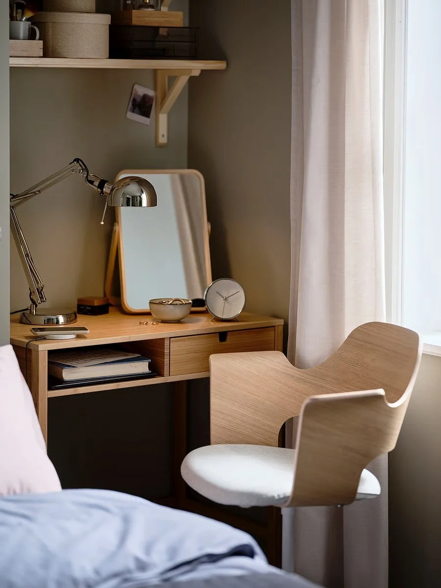 A silver IKEA FORSÅ Work Lamp with an adjustable arm and shade sits on a wooden desk next to a mirror, a small bowl, and a clock.