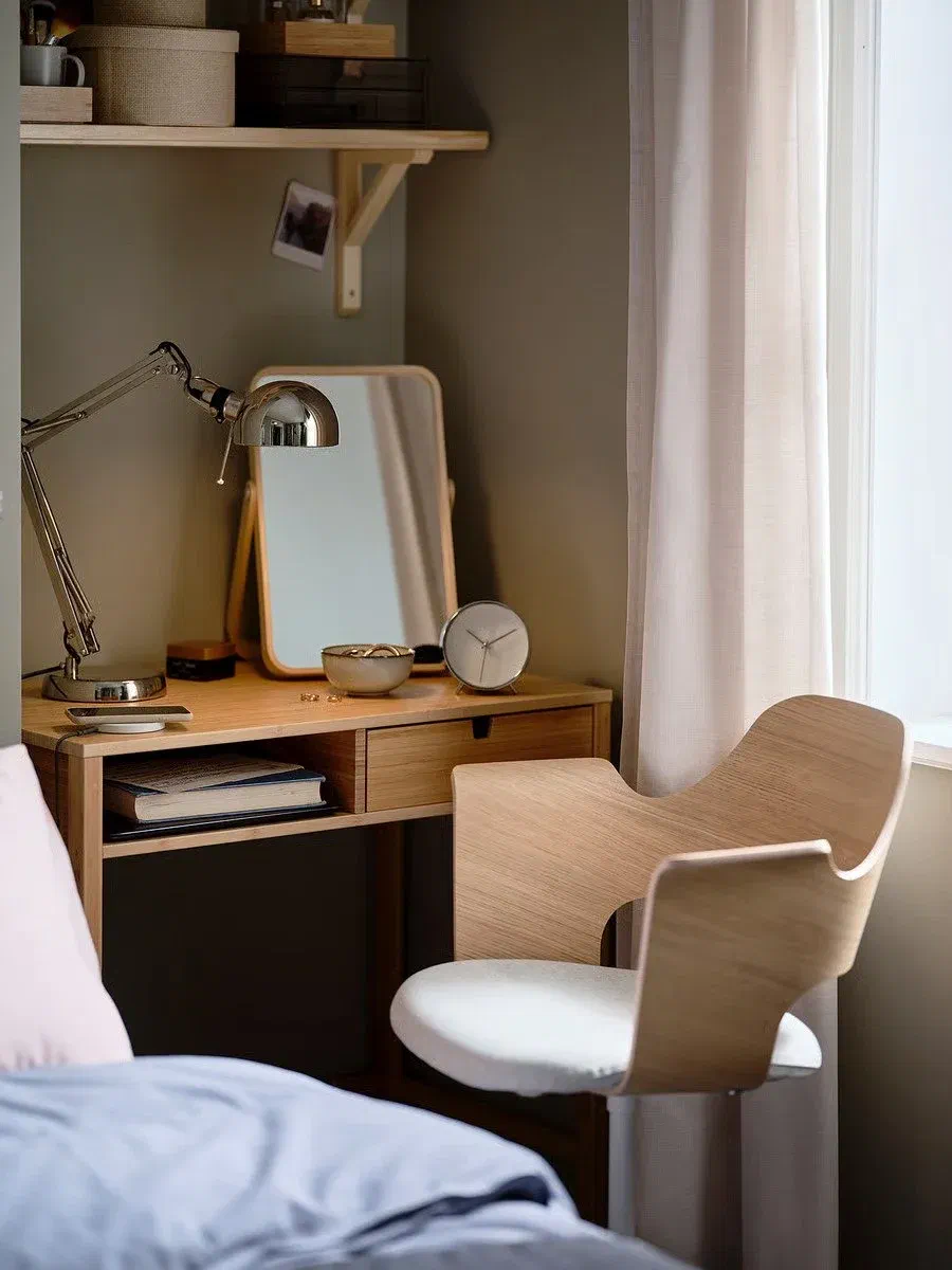 A silver IKEA FORSÅ Work Lamp with an adjustable arm and shade sits on a wooden desk next to a mirror, a small bowl, and a clock.