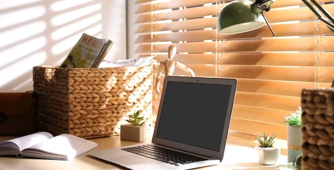 Workspace with desk lamp and natural light, showing how to avoid shadows on a desk. Laptop, books, and plants illustrate a well-lit home office.