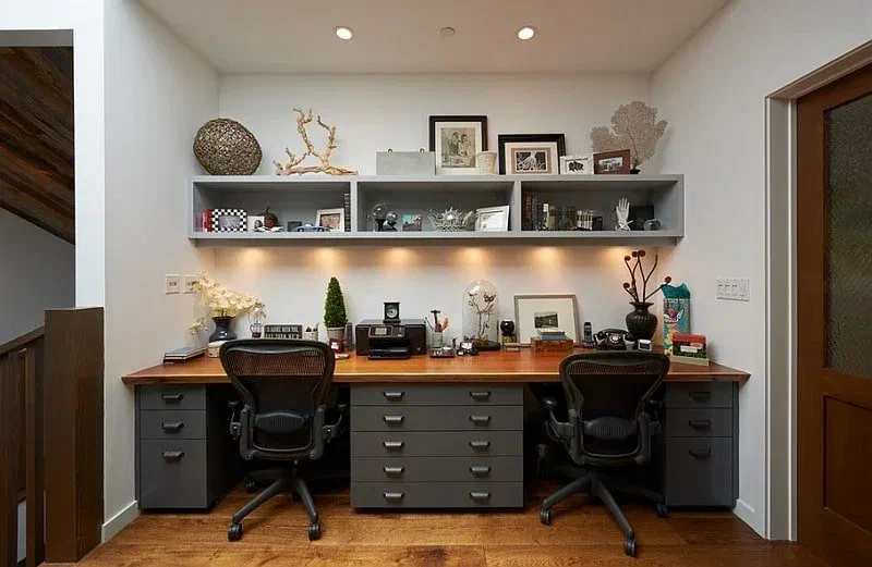 Windowless office with bright overhead lights and shelf lighting. Two desks, two chairs, and a shelf with decorations.