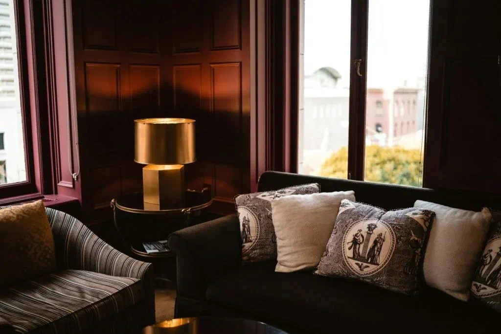 A brass, geometric table lamp adds visual interest to a dark, Victorian style interior