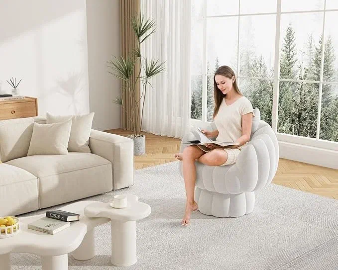 Woman reading in a plush round white swivel chair beside a cream sofa and a floor-to-ceiling window