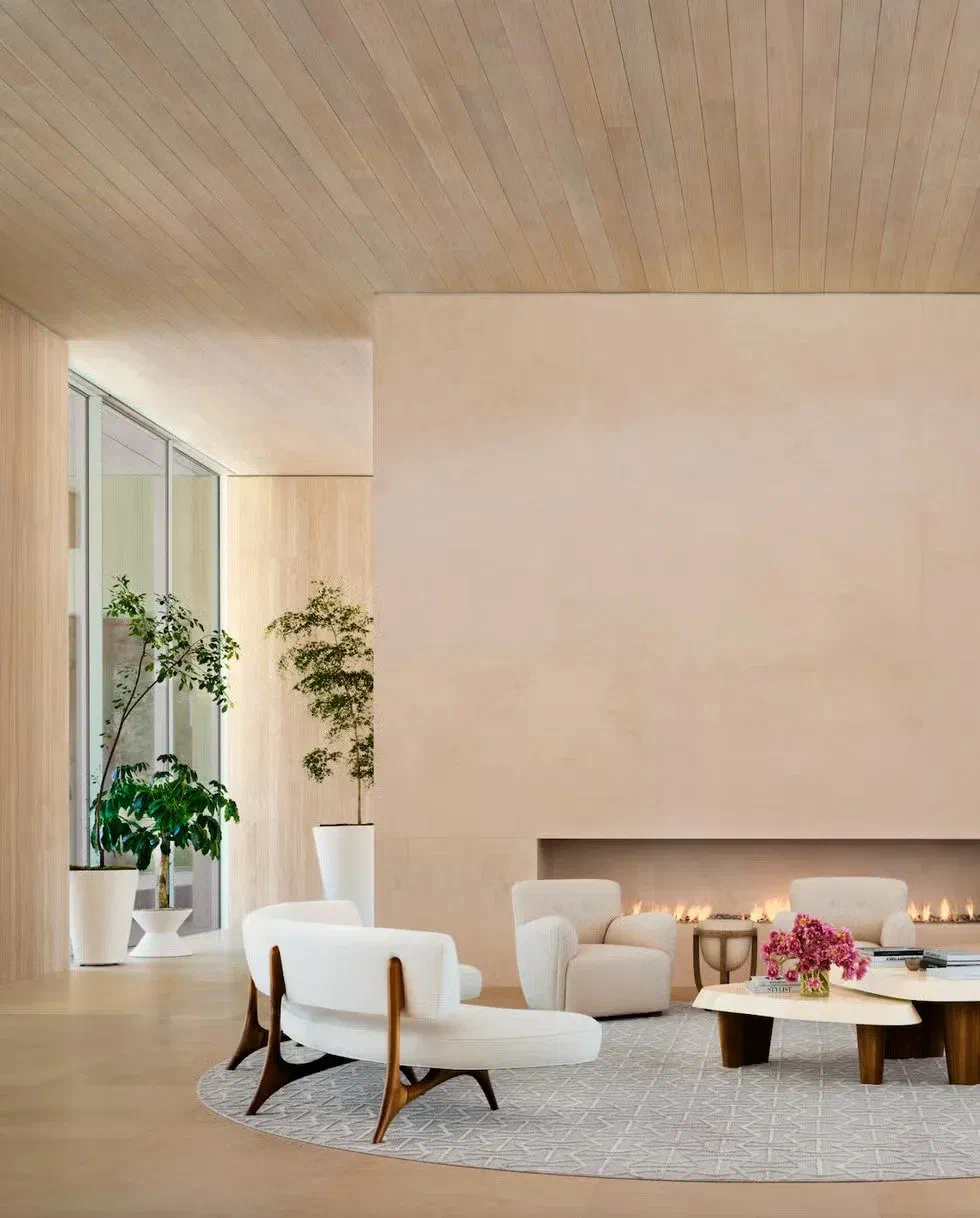 Minimalist living room with curved white lounge chairs and a linear gas fireplace set into a warm plaster wall