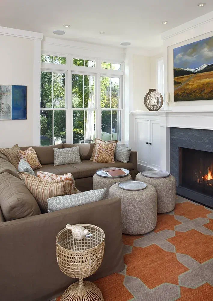 Small living room with a brown sectional, round tufted ottomans, and an orange geometric rug in front of a slate fireplace