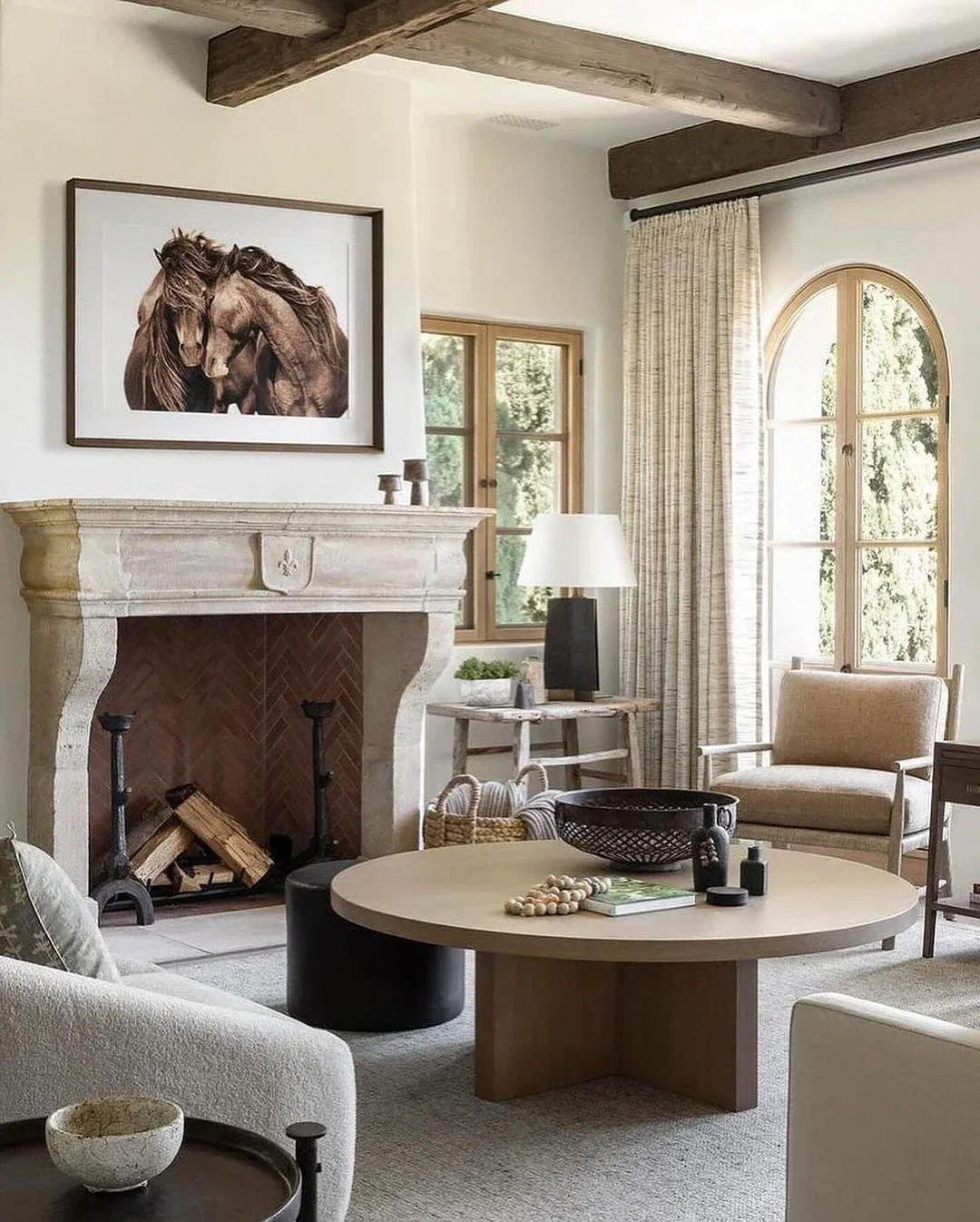 Farmhouse living room with a stone fireplace, exposed wood beams, and a round wood coffee table beside a cream sofa