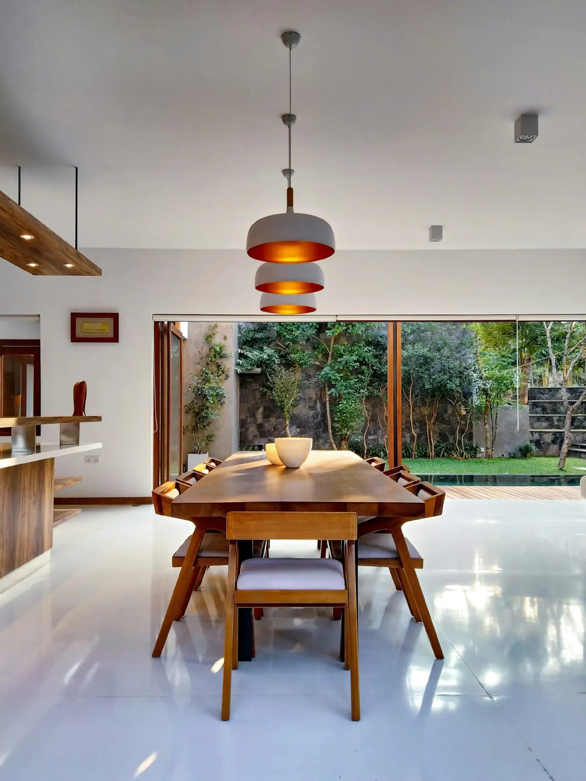 Modern dining room with a long wooden table and stylish pendant lights, offering focused illumination and a contemporary aesthetic, with natural light from large windows
